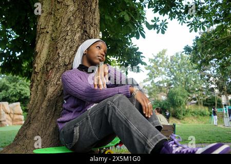 Großbritannien, London, Junge Frau im Hijab, die am Baumstamm sitzt Stockfoto