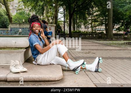 USA, lächelnde Frau mit Rollschuhen, die im Park sitzt und mit dem Smartphone spricht Stockfoto