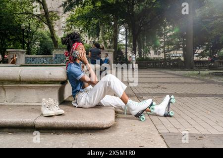 USA, Junge Frau mit Rollschuhen, die im Park sitzt und mit dem Smartphone spricht Stockfoto