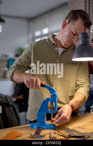 Hübscher Kerl in grauem Hemd, der den Hebel an der Druckmaschine hält, um das geprägte Logo zu bekommen. Arbeitsprozess. Arbeitszeit am Arbeitsplatz. Stockfoto