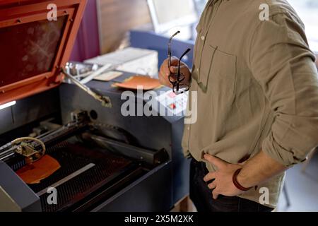 Mann mit Händen auf den Hüften, der auf dem Lasergravur arbeitet, Nahaufnahme Seitenansicht zugeschnittener Schuss Stockfoto