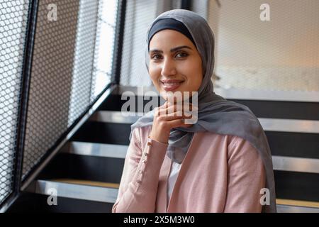 Porträt einer lächelnden Frau mit Kopftuch, die auf Stufen sitzt Stockfoto