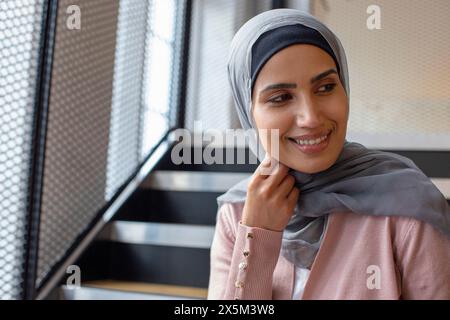 Porträt einer lächelnden Frau mit Kopftuch, die auf Stufen sitzt Stockfoto