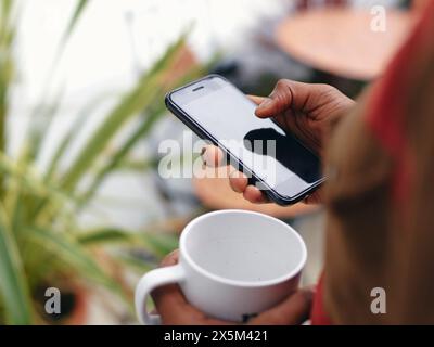 Nahaufnahme der Hände des Mannes, die Smartphone und Becher halten Stockfoto