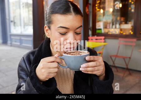 Eine mittelErwachsene Frau trinkt Kaffee im Straßencafé Stockfoto