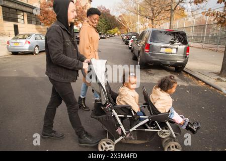 Eltern gehen auf der Straße mit Töchtern im Kinderwagen Stockfoto