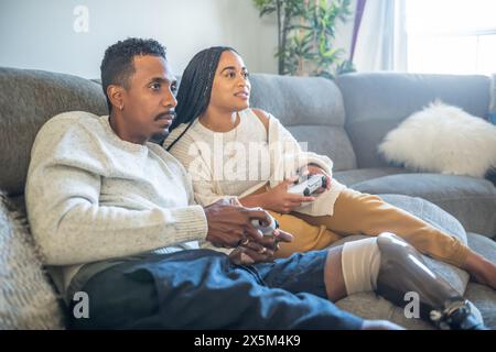 Frau und Mann mit Beinprothese spielen Videospiel auf dem Sofa Stockfoto