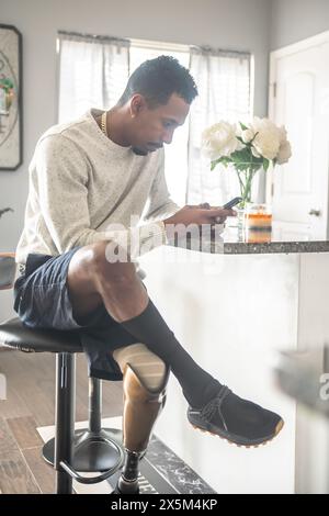 Mann mit Beinprothese mit Smartphone in der Küche Stockfoto