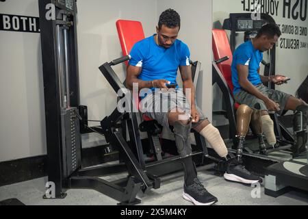 Mann mit Beinprothese, der im Fitnessstudio auf das Smartphone schaut Stockfoto