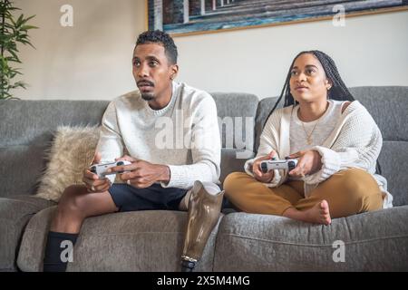 Frau und Mann mit Beinprothese spielen Videospiel auf dem Sofa Stockfoto