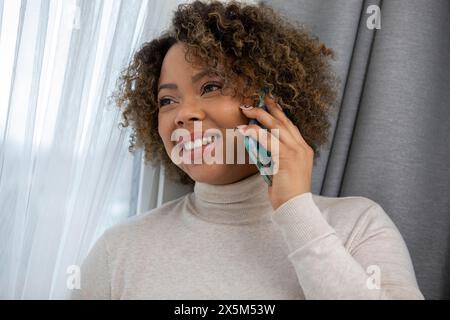 Lächelnde Frau, die am Smartphone am Fenster spricht Stockfoto