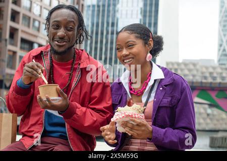 Lächelnde Freunde essen Essen in der Stadt Stockfoto