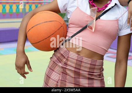 Der mittlere Teil einer jungen Frau in der Oberkante, die Basketballball hält Stockfoto