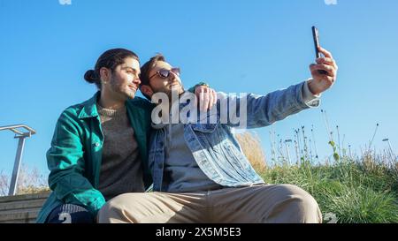 Lächelndes schwules Paar macht Selfie draußen Stockfoto