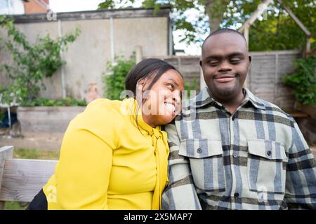 Mutter und erwachsener Sohn mit Down-Syndrom, die auf einer Bank im Garten sitzen Stockfoto