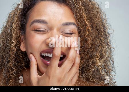 Nahaufnahme einer lächelnden Frau mit lockigen Haaren und geschlossenen Augen Stockfoto