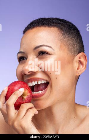 Studio-Porträt einer lächelnden Frau, die Apfel vor violettem Hintergrund hält Stockfoto