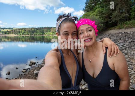 Porträt lächelnder Frauen in Badeanzügen am felsigen Seeufer in Yorkshire, Großbritannien Stockfoto