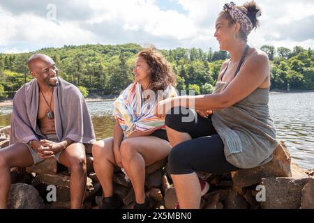 Lächelnde Freunde, in Handtücher gewickelt, sitzen am Seeufer in Yorkshire, Großbritannien Stockfoto