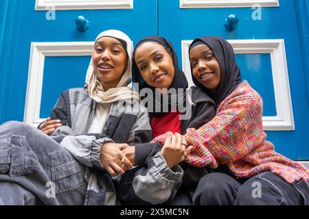 Porträt von drei lächelnden Frauen in Hijabs, die sich in der Stadt umarmen Stockfoto