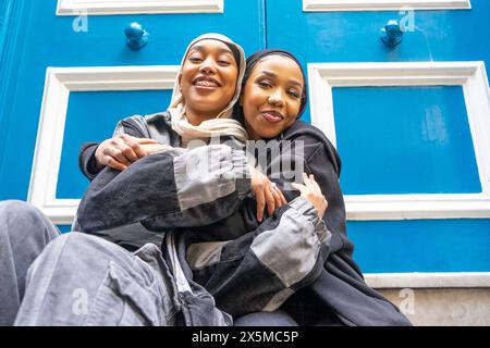 Porträt von zwei lächelnden Frauen, die Hijabs tragen, die sich in der Stadt umarmen Stockfoto