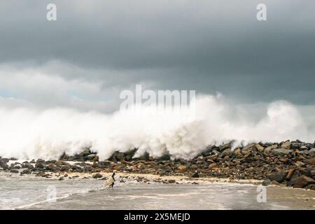 USA, Kalifornien, Morro Bay. Surfer und Wellen, die über die Felsen des Stegs krachen. Stockfoto