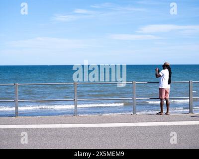 Mann, der auf der Promenade steht und das Meer fotografiert Stockfoto
