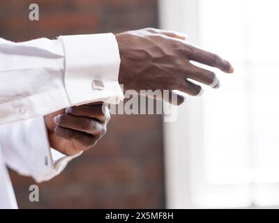 Nahaufnahme der Person, die die Manschettenknöpfe am weißen Hemdärmel befestigt Stockfoto