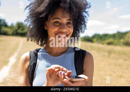 Junge Frau, die auf dem Land wandert und ihr Smartphone benutzt Stockfoto