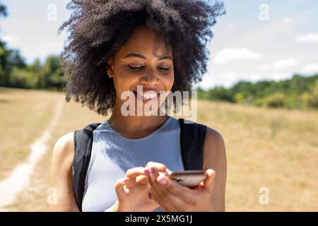 Junge Frau, die auf dem Land wandert und ihr Smartphone benutzt Stockfoto