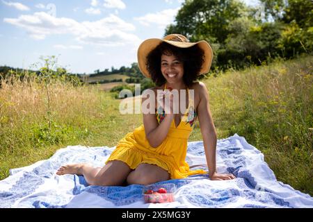 Junge Frau, die auf einer Decke auf der Wiese sitzt Stockfoto