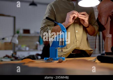 Ein junger Mann macht Löcher für die Knöpfe auf einer speziellen Montagepresse. Nahaufnahme zugeschnittener Shot. Hand Drücken Stockfoto