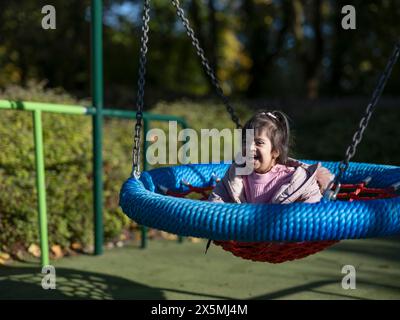 Mädchen mit Down-Syndrom, das auf dem Spielplatz in Schaukel sitzt Stockfoto