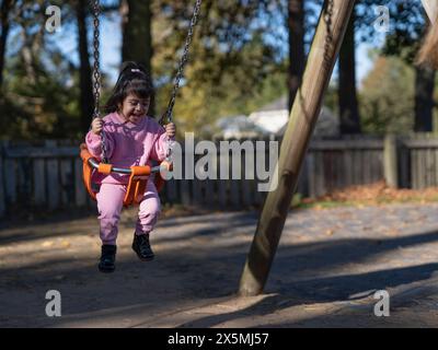 Mädchen mit Down-Syndrom schwingt auf dem Spielplatz Stockfoto