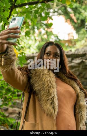 Schwangere Frau im Mantel, die im Herbst Selfie im Park macht Stockfoto