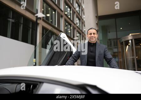 Ein lächelnder reifer Mann, der sich an ein Luxusauto lehnt Stockfoto