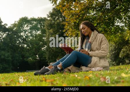 Frau im Mantel liest im Herbst Buch im Park Stockfoto