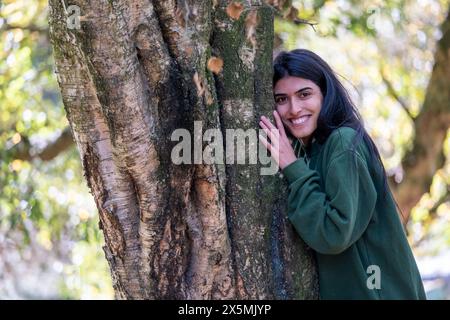 Porträt einer lächelnden Frau, die einen Baum im Wald berührt Stockfoto