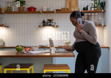 Schwangere Frau telefonieren mit Handy in Küche Stockfoto