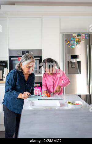 Eine ältere Frau mit Enkelin, die Gemüse in der Küche hackt Stockfoto