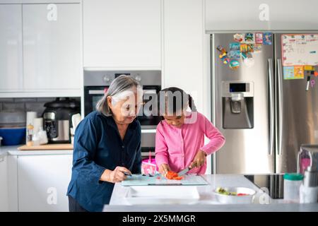 Eine ältere Frau mit Enkelin, die Gemüse in der Küche hackt Stockfoto