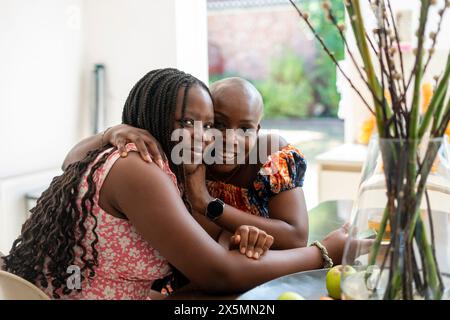 Porträt einer lächelnden Mutter und Tochter im Teenageralter, die sich am Tisch umarmen Stockfoto