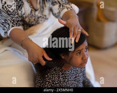 Mutter macht Töchterhaare, während sie fernsieht Stockfoto