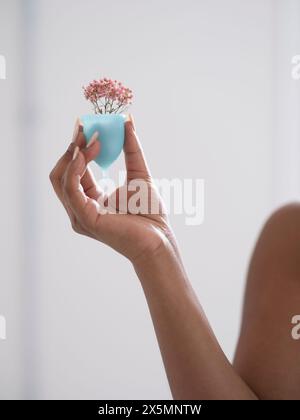 Nahaufnahme einer Frauenhand, die Menstruationstasse mit Blumen hält Stockfoto