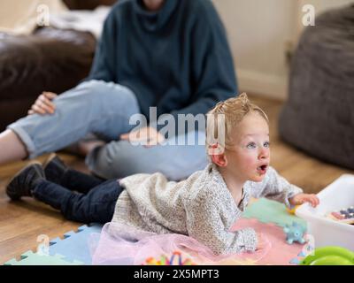 Junge mit Zerebralparese spielt auf der Matte, Mutter im Hintergrund Stockfoto