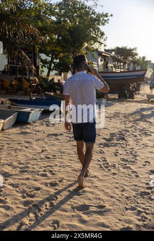 Mann, der am Strand entlang läuft und telefoniert Stockfoto