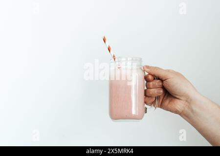 Eine Hand, die einen Erdbeer-Smoothie-Krug auf weißem Hintergrund hält Stockfoto