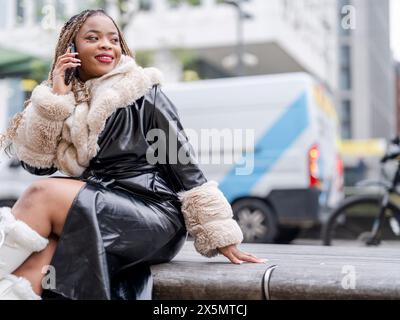 Lächelnde junge Frau, die auf der Straße telefoniert Stockfoto
