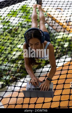 Frau, die sich am Netz entspannt und ein Notebook mit Kopfhörern benutzt Stockfoto