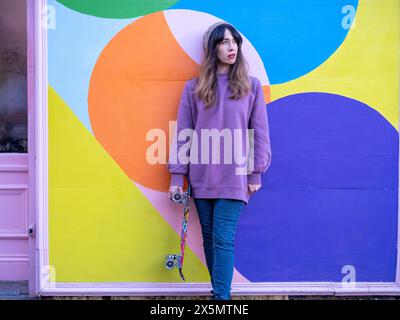 Porträt einer Frau, die mit Skateboard gegen mehrfarbige Wand steht Stockfoto
